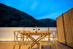 A table with two chairs, a bottle, and two glasses on a balcony with a view of a forested hill. - Hotel Senkei (Hakone)