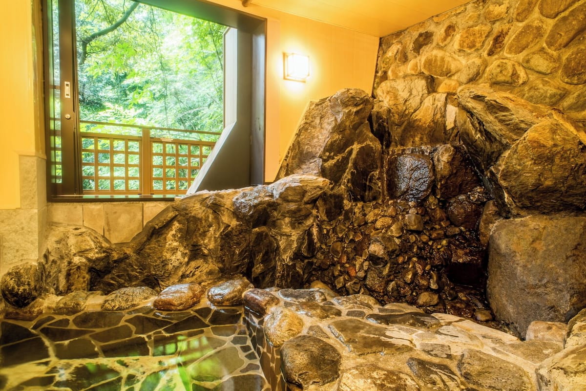 A stone wall with a water feature, a window with a view of greenery, and a stone floor.