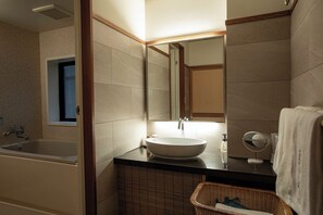 A bathroom with a bathtub, a sink, a mirror, and a wicker basket. - Hotel Senkei (Hakone)