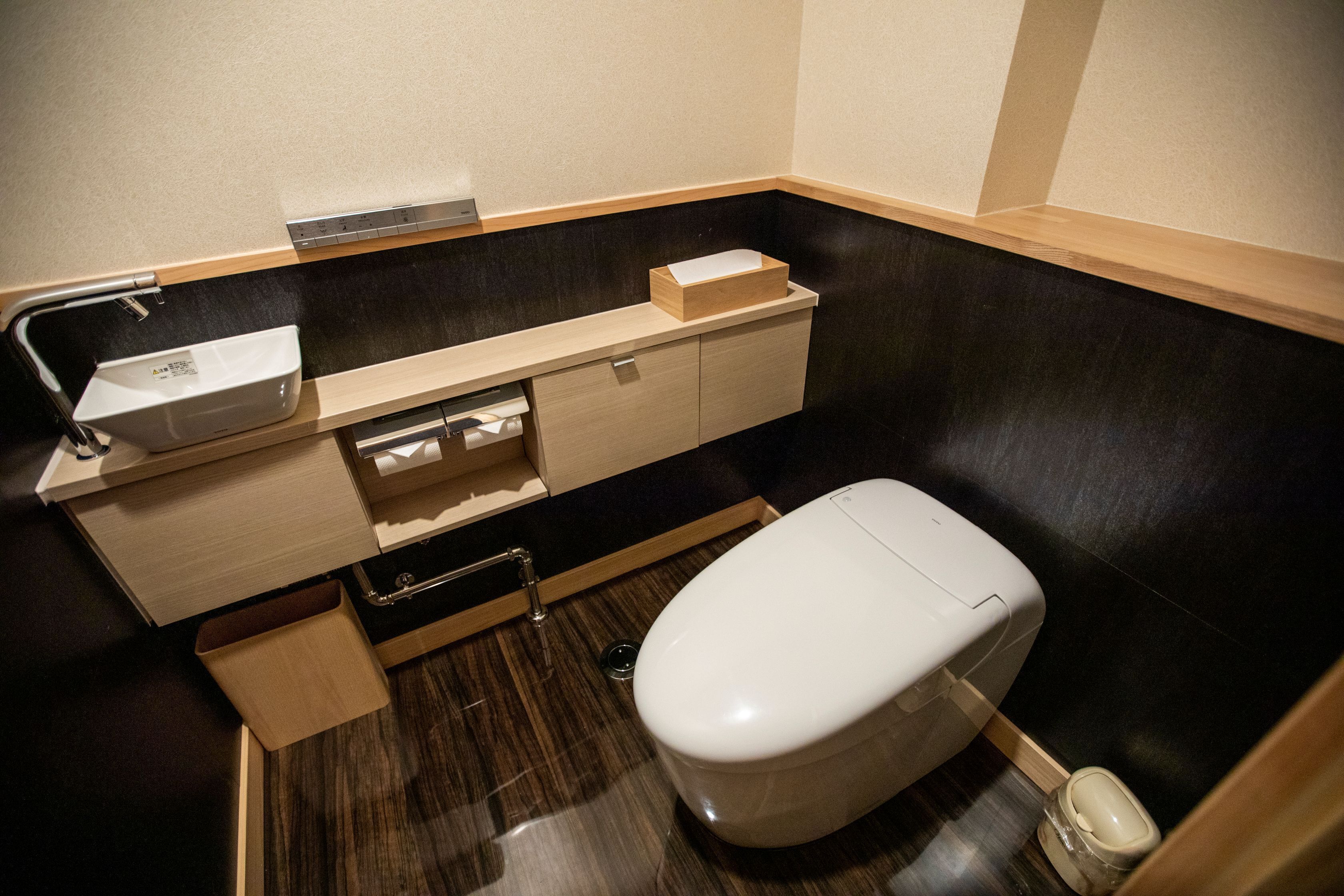 Et lille badeværelse med toilet, vask og et mindre skab.
