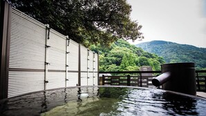 Zona de aguas termales con cerca de madera, baranda metálica y vista a una montaña boscosa.