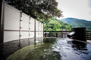 A hot spring area with a wooden fence, a metal railing, and a view of a forested mountain. - Hotel Senkei (Hakone)