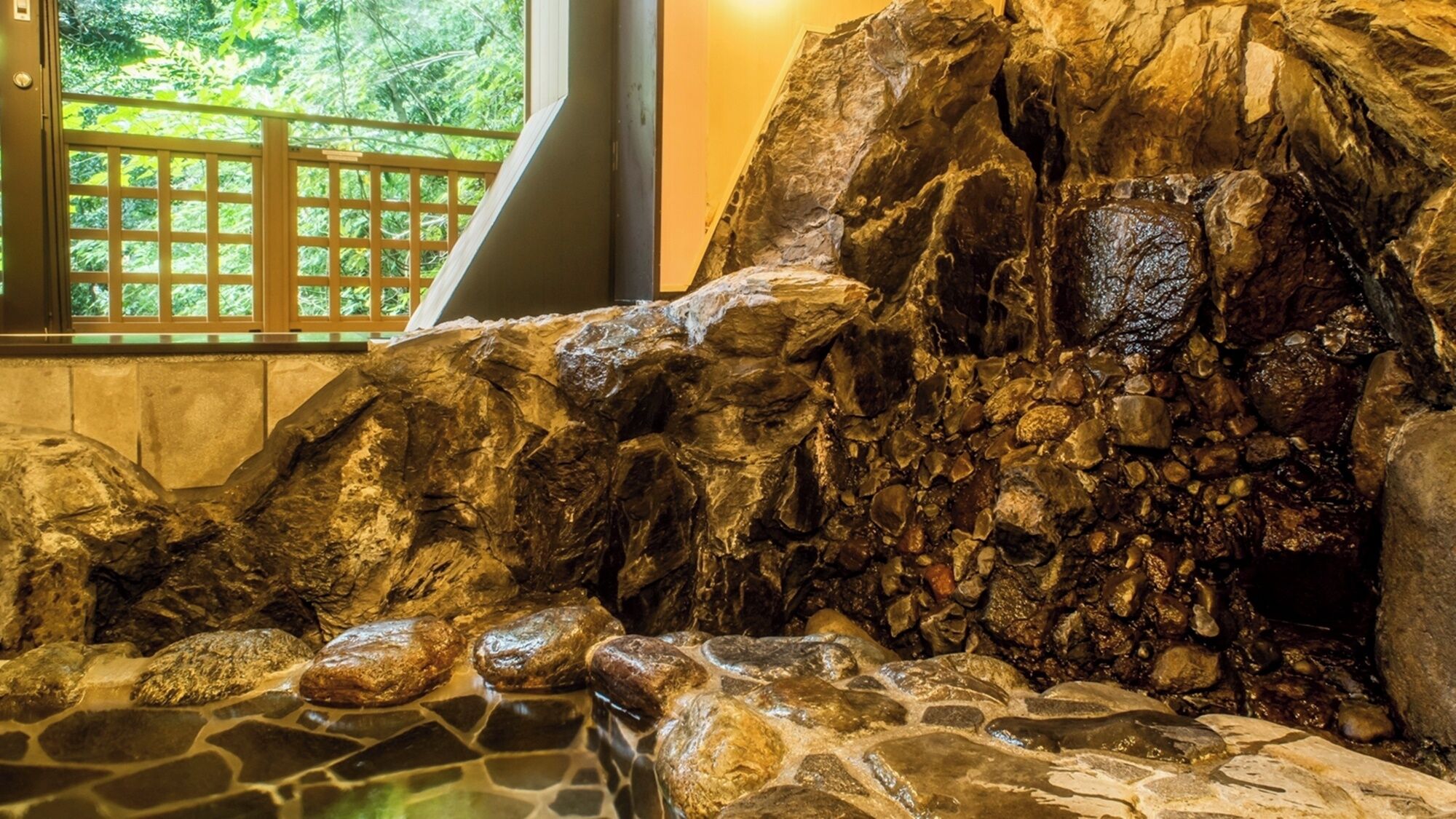A rock formation with a water feature, a wooden fence, and a window with a view of greenery.