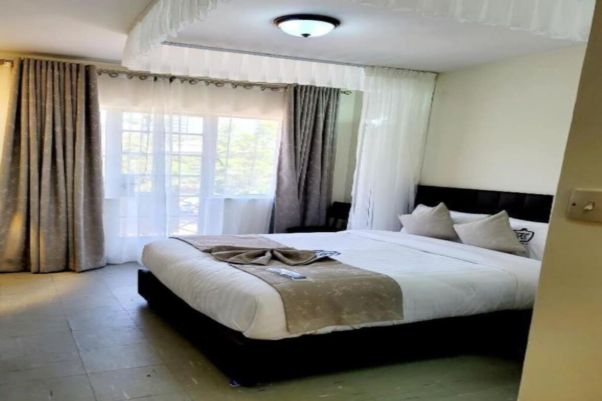 Quarto de hotel com uma cama grande, cabeceira e janela com cortinas.