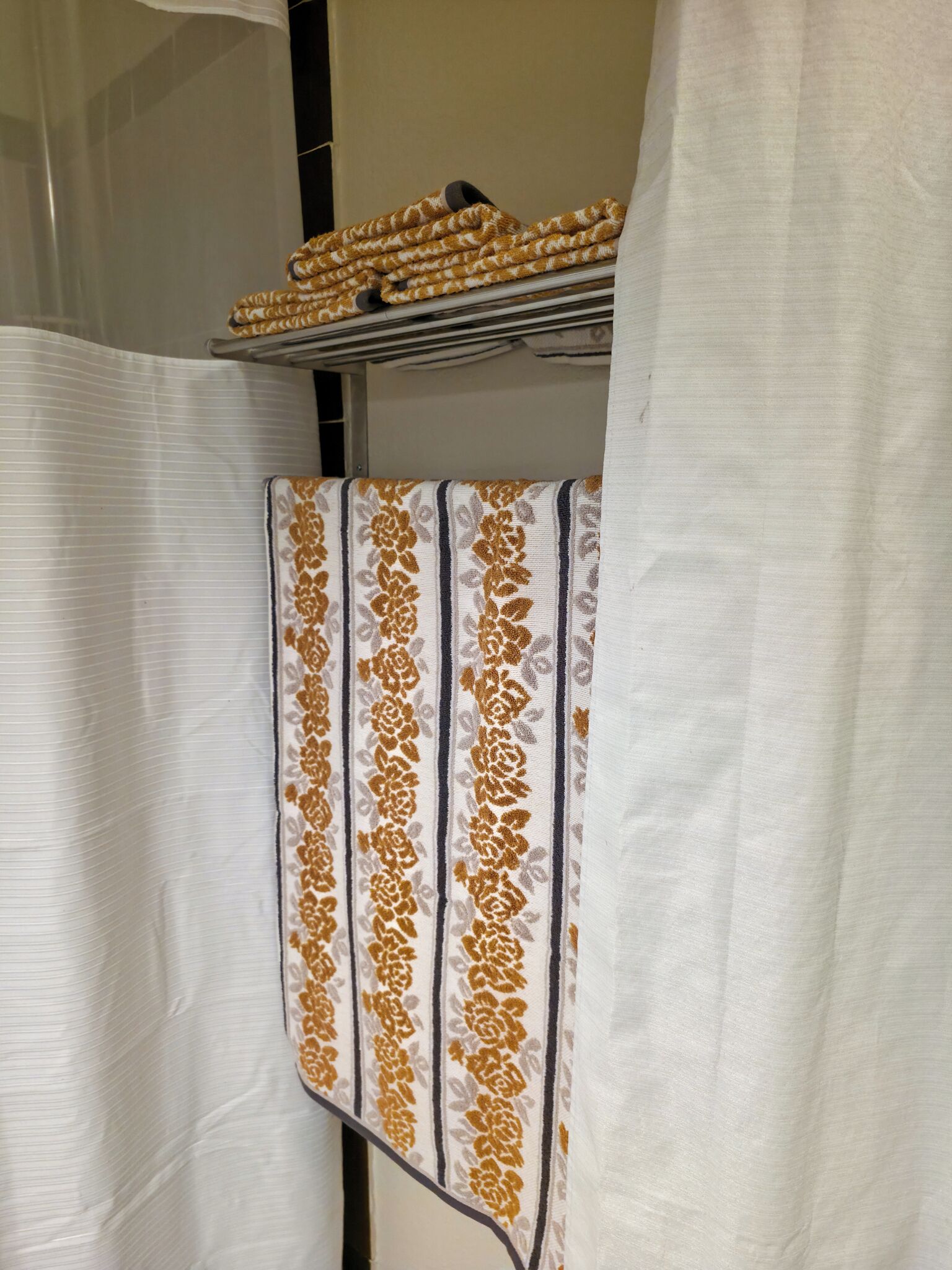 A bathroom with a white shower curtain, a towel rack with folded towels, and a striped towel.