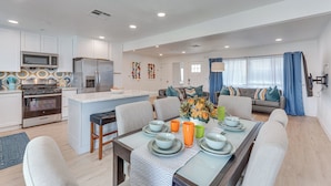 A modern kitchen with white cabinets, a microwave, and a refrigerator. There is a dining area with a table set for four, including plates, bowls, and glasses. - Palm Springs Oasis | Poolside Retreat (Palm Springs)