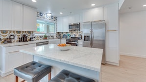 A modern kitchen with white cabinets, a marble countertop, and stainless steel appliances. - Palm Springs Oasis | Poolside Retreat (Palm Springs)