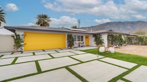 A residential property with a yellow garage, a well-maintained lawn, and a mountainous backdrop. - Palm Springs Oasis | Poolside Retreat (Palm Springs)