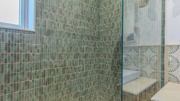 Un baño con ducha de vidrio, paredes con azulejos, ventana y tocador de madera.
