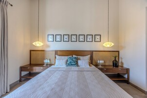 A neatly arranged hotel room with a large bed, two bedside tables, a headboard with a woven pattern, and framed pictures on the wall.