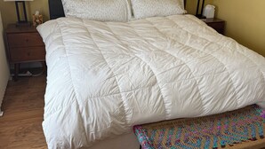 Un dormitorio con una cama grande, dos mesitas de noche con lámparas, un banco y una alfombra estampada.