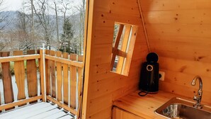 Une cabane en bois avec une terrasse, une petite fenêtre, un évier et une cuisinière à gaz.