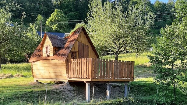 Une maison en bois avec un toit de chaume, construite sur pilotis au-dessus d’une étendue d’eau, entourée de verdure et d’arbres.