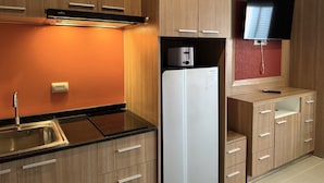 A modern kitchen with wooden cabinets, a black countertop, a white refrigerator, a toaster, and a flat-screen TV mounted on the wall. - Modern Studio With Balcony and Pool - Pratumnak Hill (Pattaya)