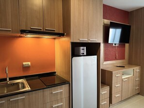 A modern kitchen with wooden cabinets, a black countertop, a white refrigerator, a toaster, and a flat-screen TV mounted on the wall. - Modern Studio With Balcony and Pool - Pratumnak Hill (Pattaya)