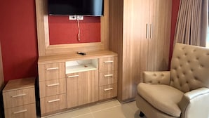 A room with a TV mounted on a wooden cabinet, a beige armchair, and a wardrobe. - Modern Studio With Balcony and Pool - Pratumnak Hill (Pattaya)