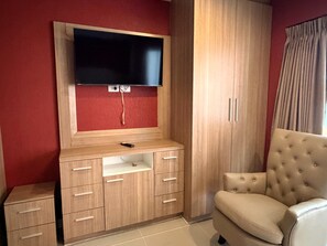 A room with a TV mounted on a wooden cabinet, a beige armchair, and a wardrobe. - Modern Studio With Balcony and Pool - Pratumnak Hill (Pattaya)