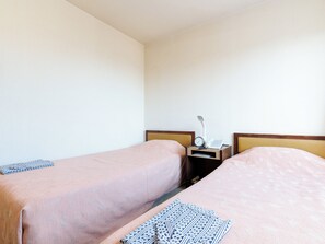 Une chambre d’hôtel avec deux lits simples, une table de chevet avec une lampe, une horloge et un téléphone.