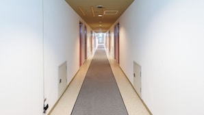 Un long couloir étroit, avec des portes de chaque côté, un sol recouvert de moquette et des spots encastrés au plafond.