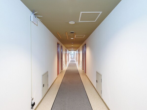 Un long couloir étroit, avec des portes de chaque côté, un sol recouvert de moquette et des spots encastrés au plafond.