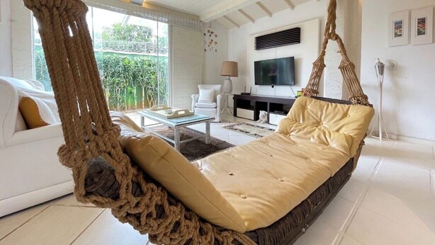 A modern living room with a hanging hammock, a sofa, a TV, and a dining area. - House in Búzios (Geribá) a few meters from the beach. (Armação dos Búzios)