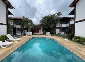 A swimming pool with lounge chairs and tables, surrounded by buildings with tiled roofs and palm trees. - House in Búzios (Geribá) a few meters from the beach. (Armação dos Búzios)