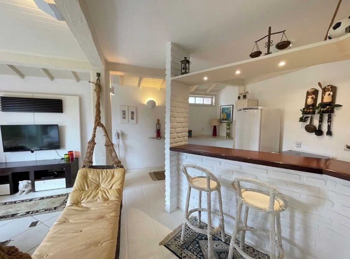 A modern living room with a sofa, a TV, and a hanging chair. There is a kitchen area with a bar and stools.