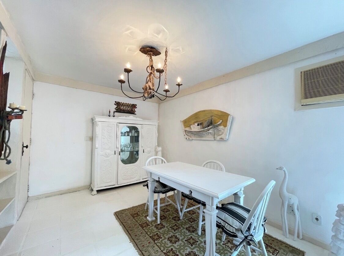 A dining area with a white table and chairs, a chandelier, a cabinet with glass doors, and wall-mounted decorations.