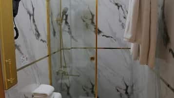 Un bany amb parets de marbre, dutxa envidriada, vàter i rentapelats.