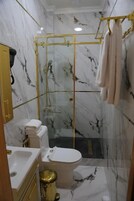 A bathroom with marble walls, a glass-enclosed shower, a toilet, and a sink.