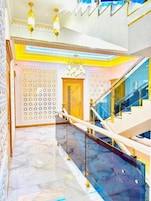 A grand staircase with a marble floor leading to a landing with a decorative wall and a chandelier.