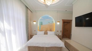 A bedroom with a large bed, a TV mounted on the wall, and a decorative archway. - Turon Khiva (Khiva)
