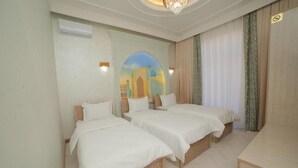 A hotel room with three single beds, a wooden desk, and a mural of a building on the wall. - Turon Khiva (Khiva)