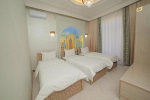 A hotel room with three single beds, a wooden desk, and a mural of a building on the wall.