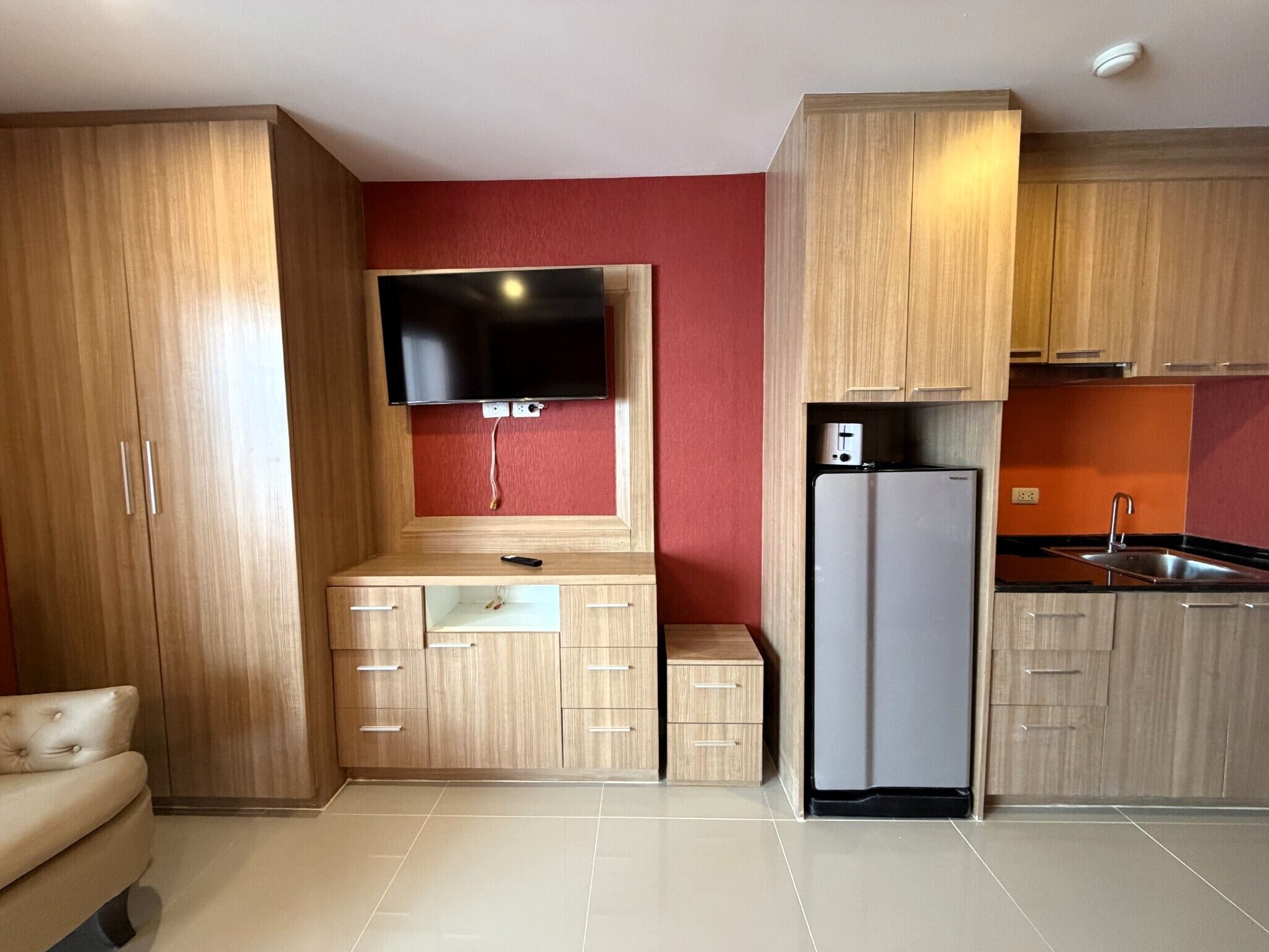 A compact kitchen with wooden cabinets, a built-in TV, a refrigerator, and a small countertop.