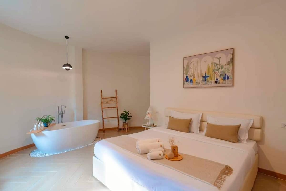 Een moderne slaapkamer met een groot bed, een badkuip en een schilderij aan de wand.
