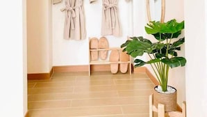 A hallway with two beige robes hanging on wooden hooks, a wooden shoe rack with shoes, a large mirror, and a potted plant. - Rabbit Villa Bangsaray (Sattahip)