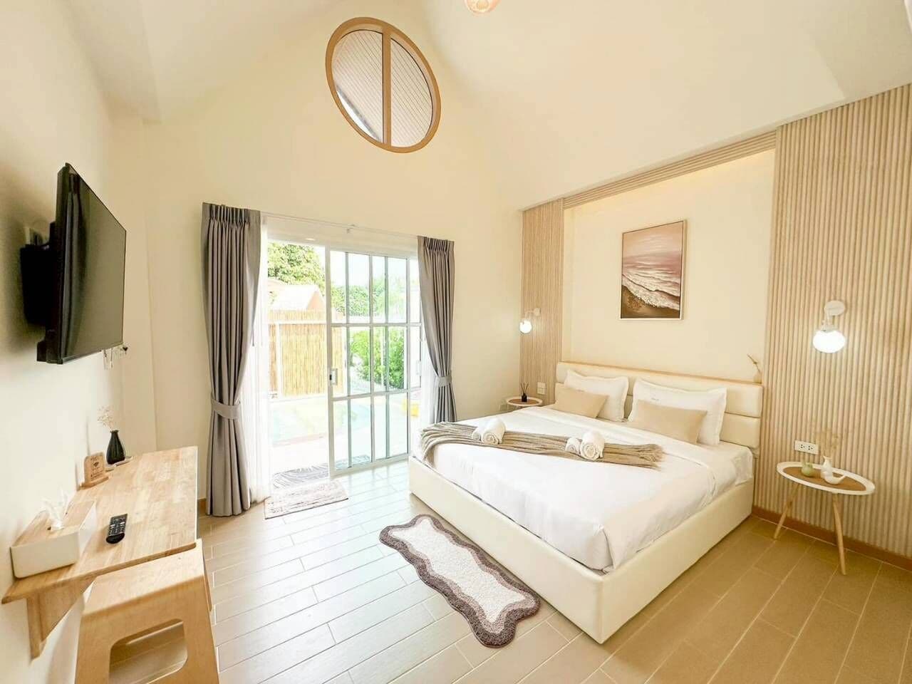 A bedroom with a bed, a desk, a TV, and a sliding glass door to the outdoors.