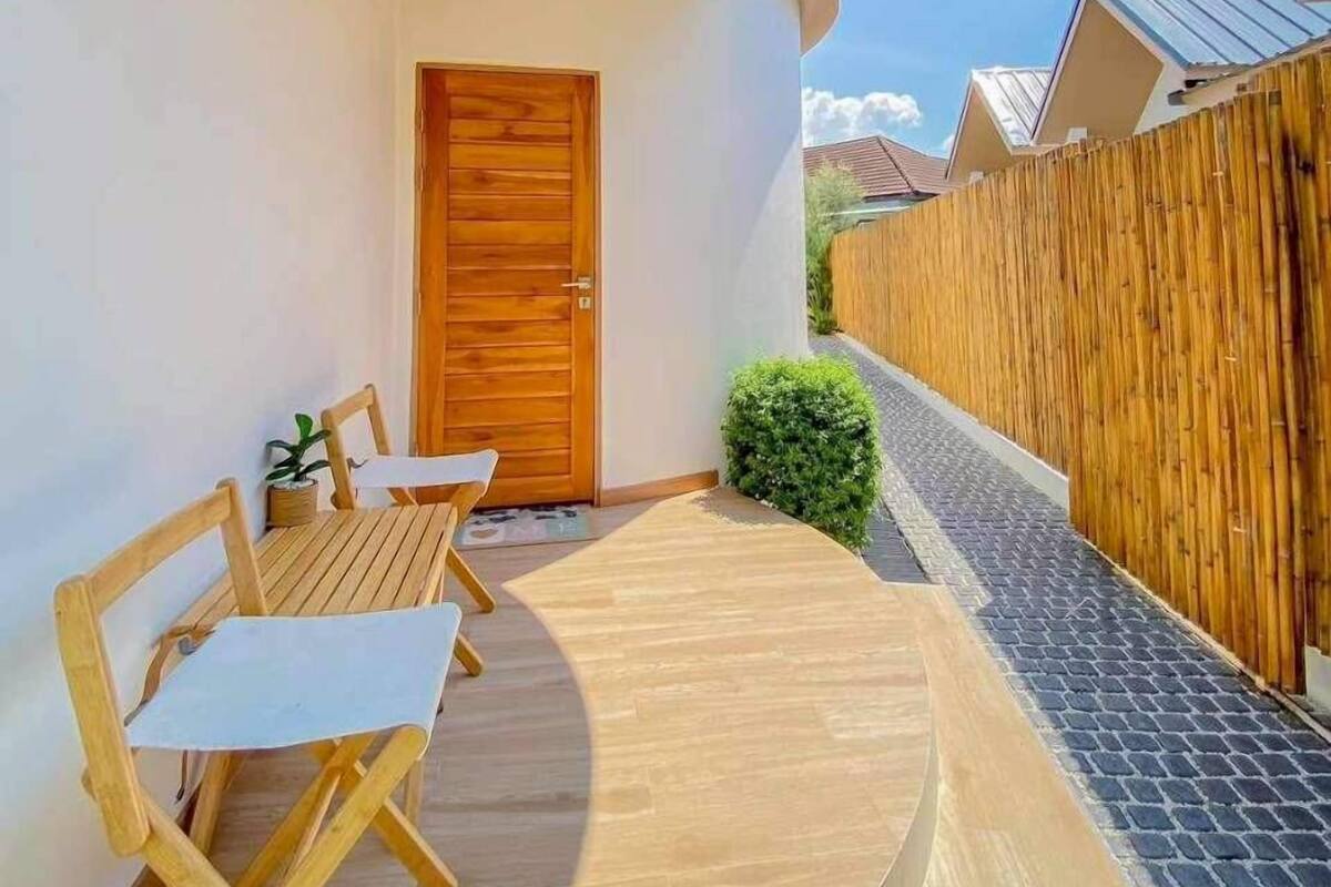 Een klein balkon met een houten deur, een tafel met stoelen en een bamboe hek.