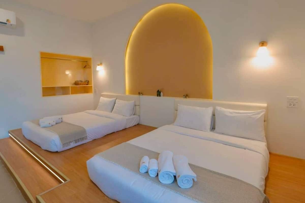 Een hotelkamer met een groot bed, twee kleinere bedden, een houten vloer, een spiegel en een wandlamp.