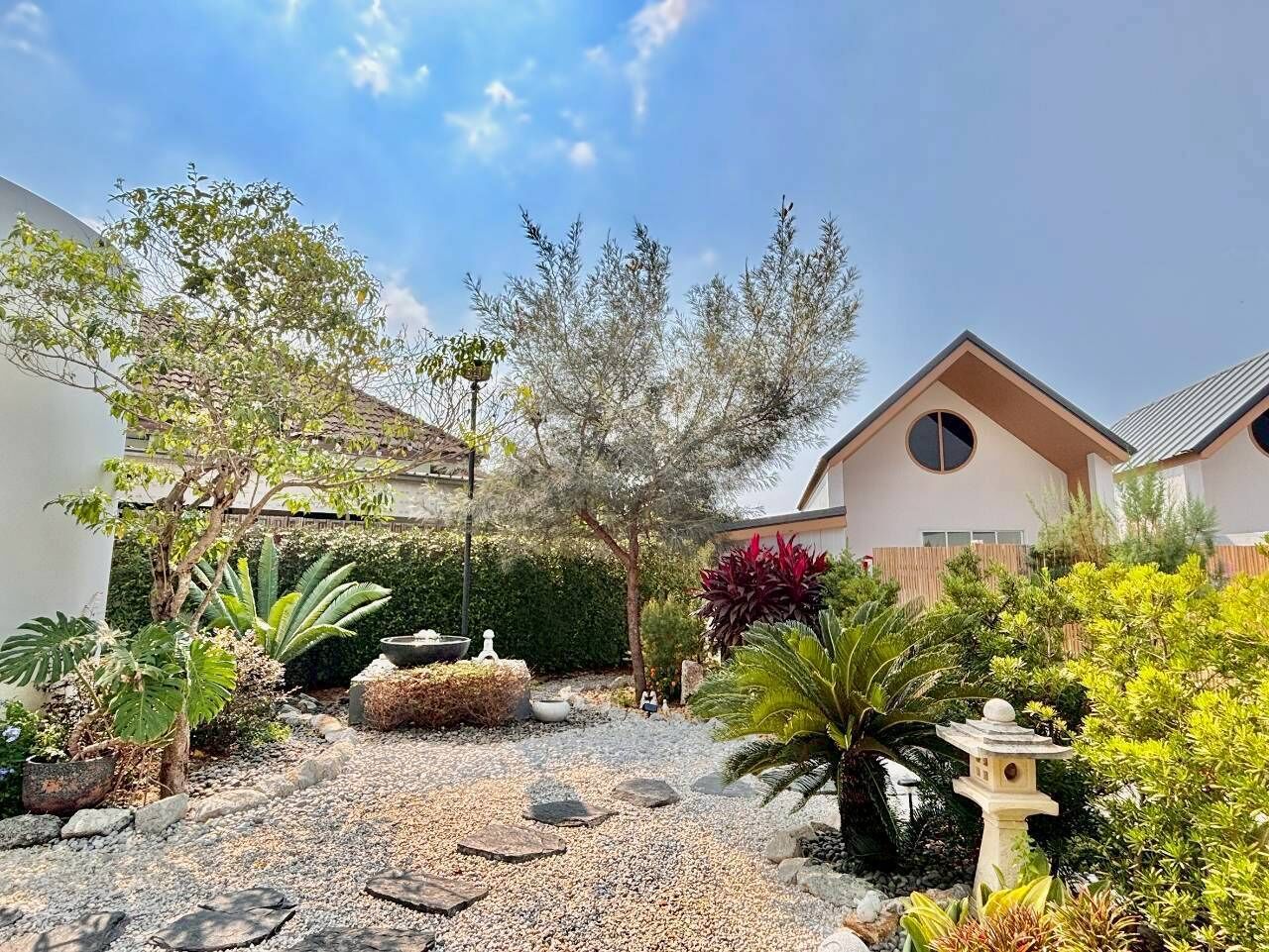 A garden with a variety of plants and a stone lantern. There are two buildings with a modern design.