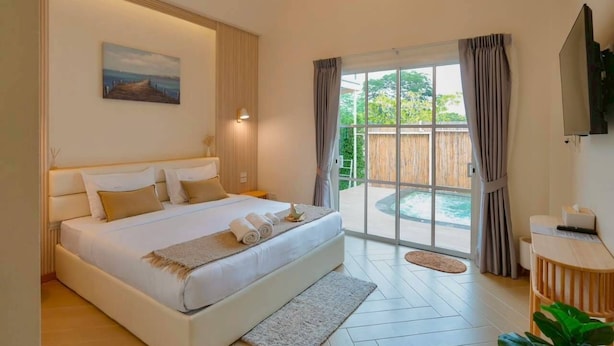 A spacious bedroom with a large bed, a painting on the wall, a television, and a view of a pool through a glass door. - Rabbit Villa Bangsaray (Sattahip)