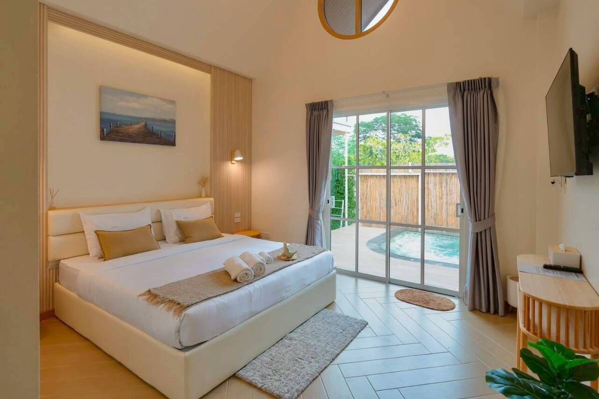 Ruime slaapkamer met een groot bed, een schilderij aan de muur, een televisie en uitzicht op een zwembad door een glazen deur.