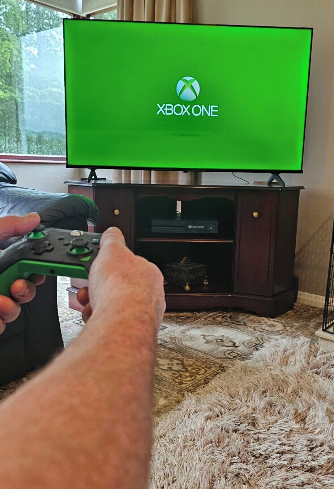 A person holding a green Xbox controller in front of a television displaying the Xbox logo.