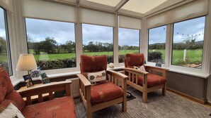 A conservatory with two wooden chairs, a table, and a lamp. - Hot Tub Cottage Near Mourne Mountains | Sleeps 6 + Infants, Pet-Friendly (Ballyward)