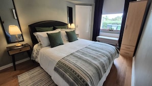 A neatly arranged bedroom with a bed, bedside lamps, a bench, and a view of the outdoors. - Hot Tub Cottage Near Mourne Mountains | Sleeps 6 + Infants, Pet-Friendly (Ballyward)