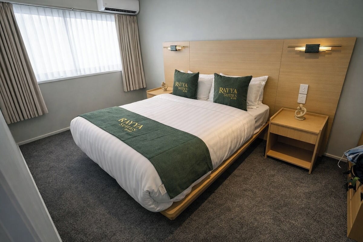 A hotel room with a bed, a nightstand, a lamp, a power outlet, and a window with curtains.