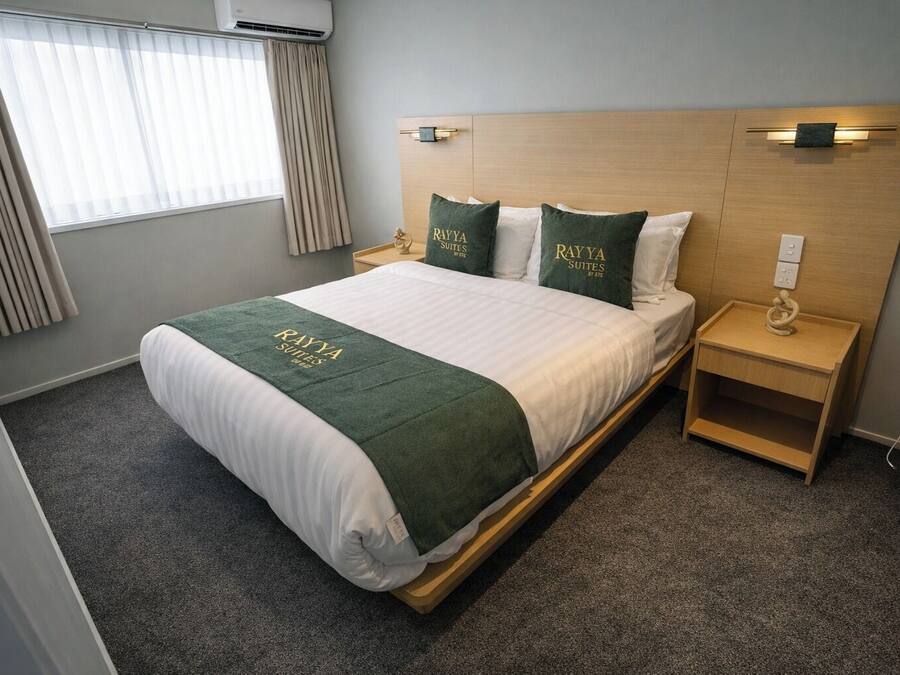 A hotel room with a bed, a nightstand, a lamp, a power outlet, and a window with curtains.