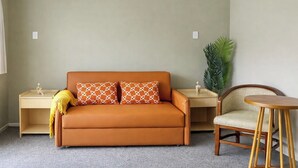 A room with a sofa, two nightstands, a chair, and a potted plant. - Rayya Suites, Paihia (Paihia)