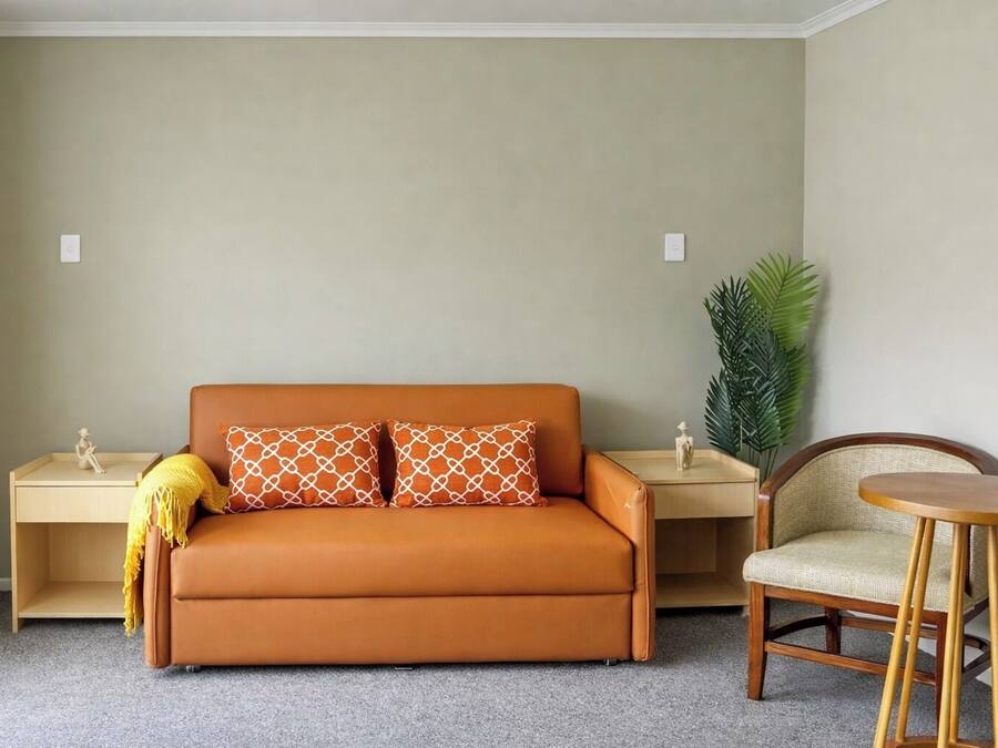 A room with a sofa, two nightstands, a chair, and a potted plant.